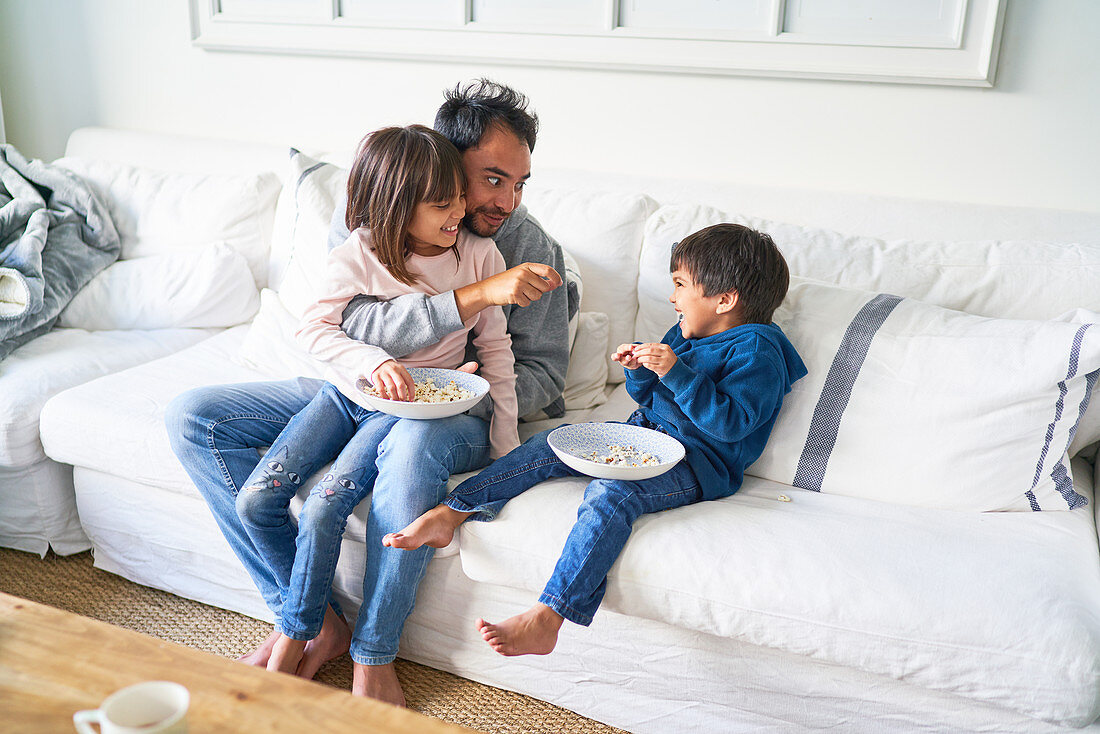 Father and kids eating popcorn on living room sofa