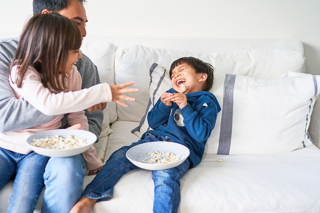 Playful family with popcorn on living room sofa
