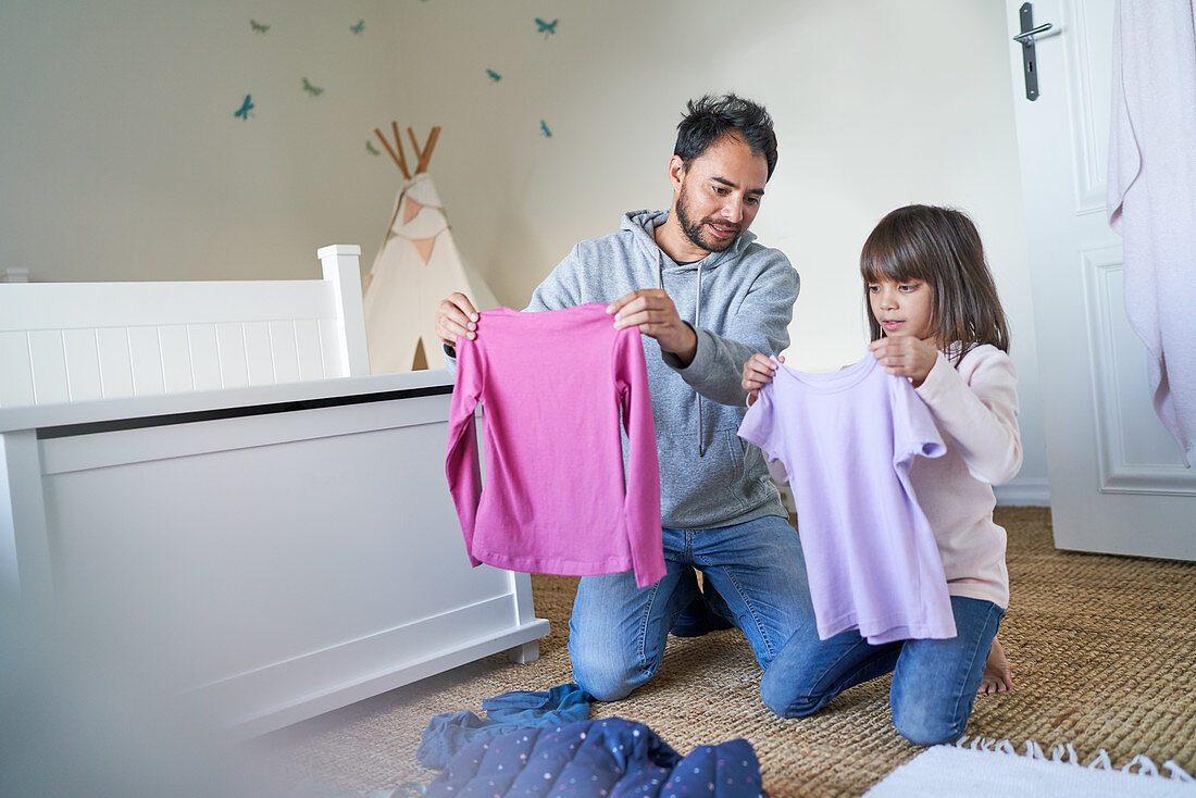 Father and daughter folding clothes in bedroom