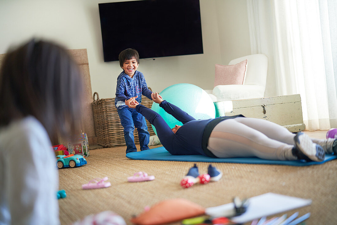 Boy playing with mother exercising on yoga mat