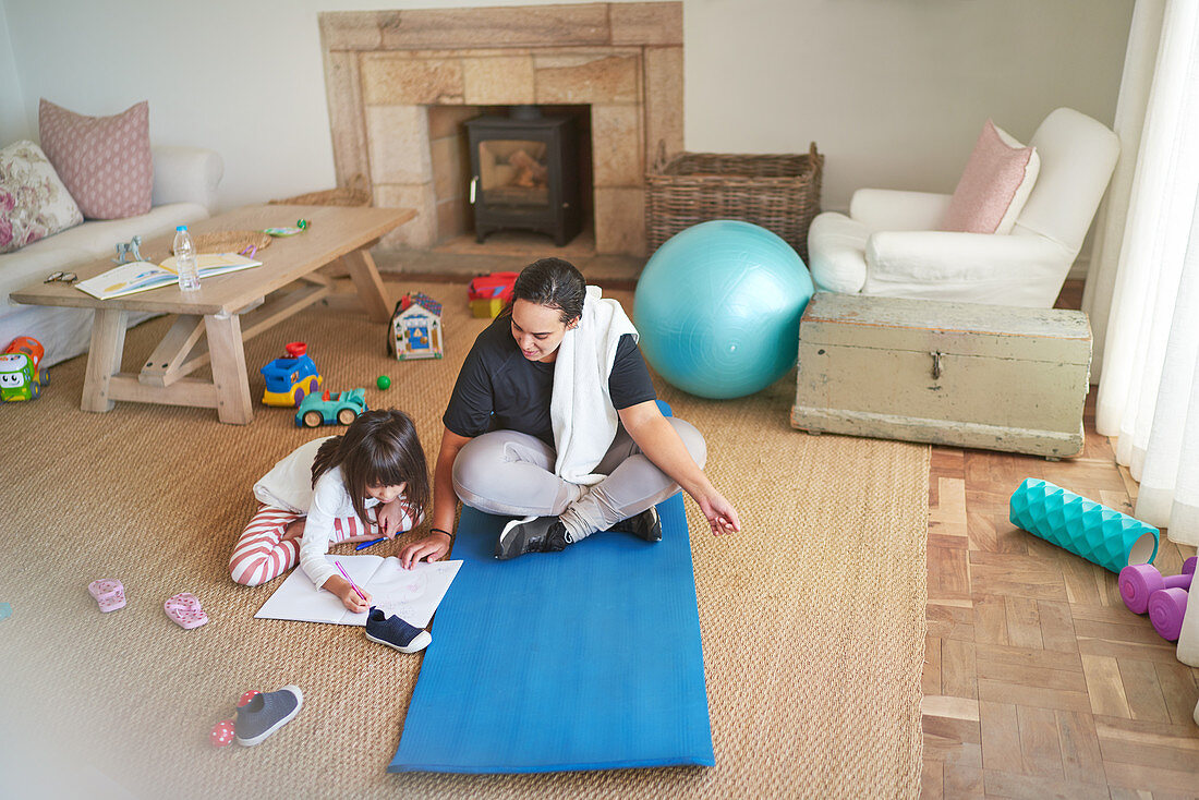 Mother on yoga mat watching daughter colouring