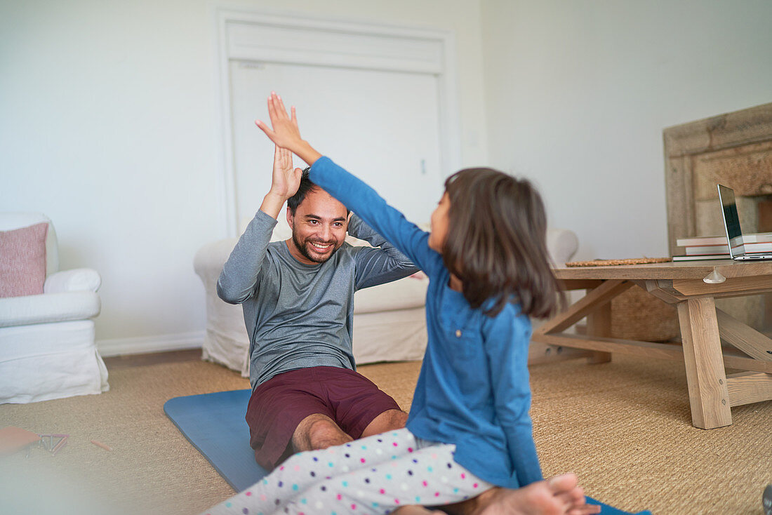 Happy father and daughter high-fiving on yoga mat