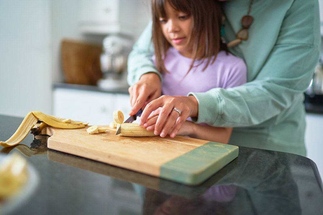 Mother helping daughter cut banana in kitchen