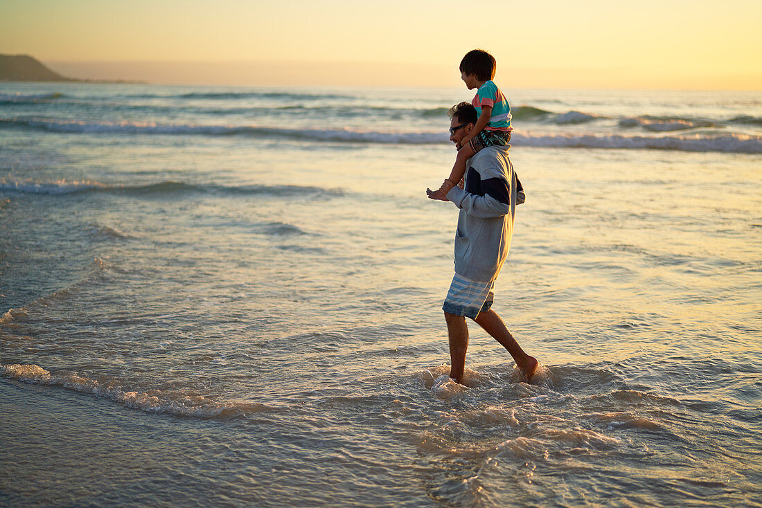 Father carrying son on shoulders in ocean surf
