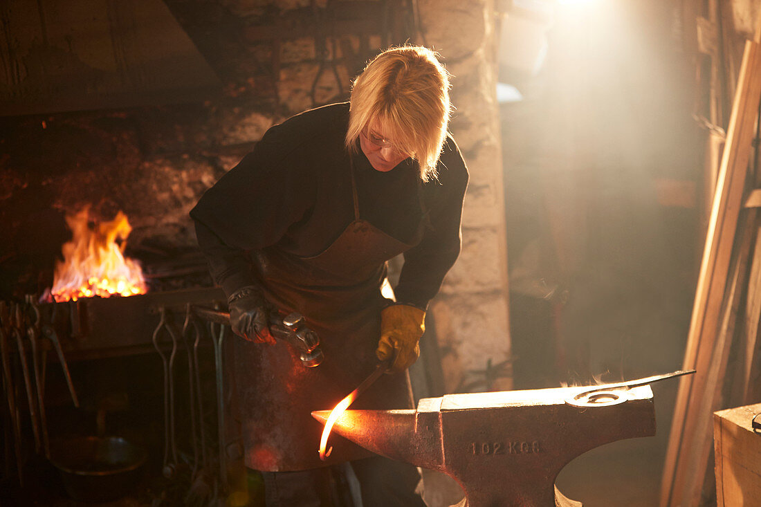 Female blacksmith forging steel in workshop