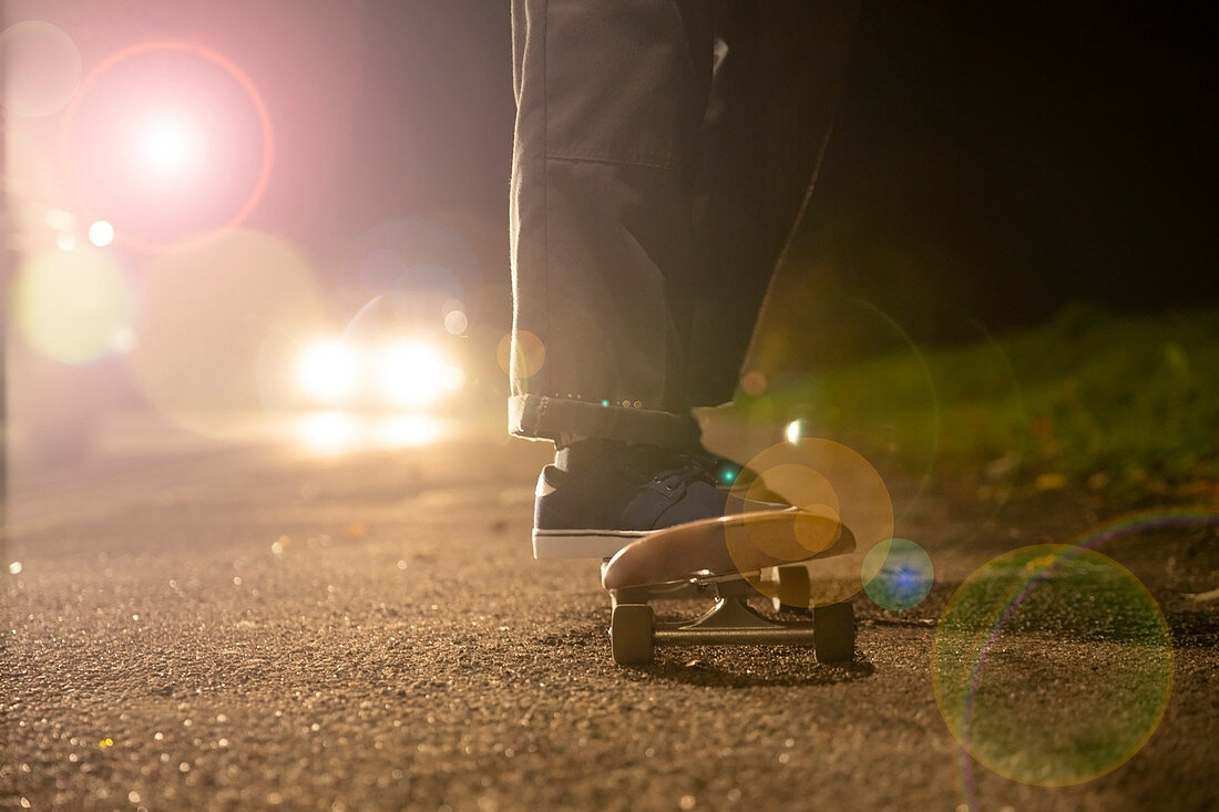 Young man skateboarding in headlights on roadside