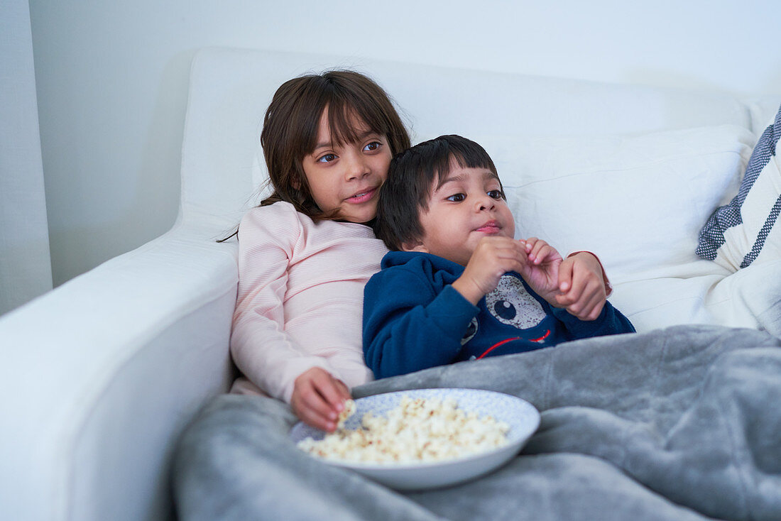 Brother and sister eating popcorn and watching TV