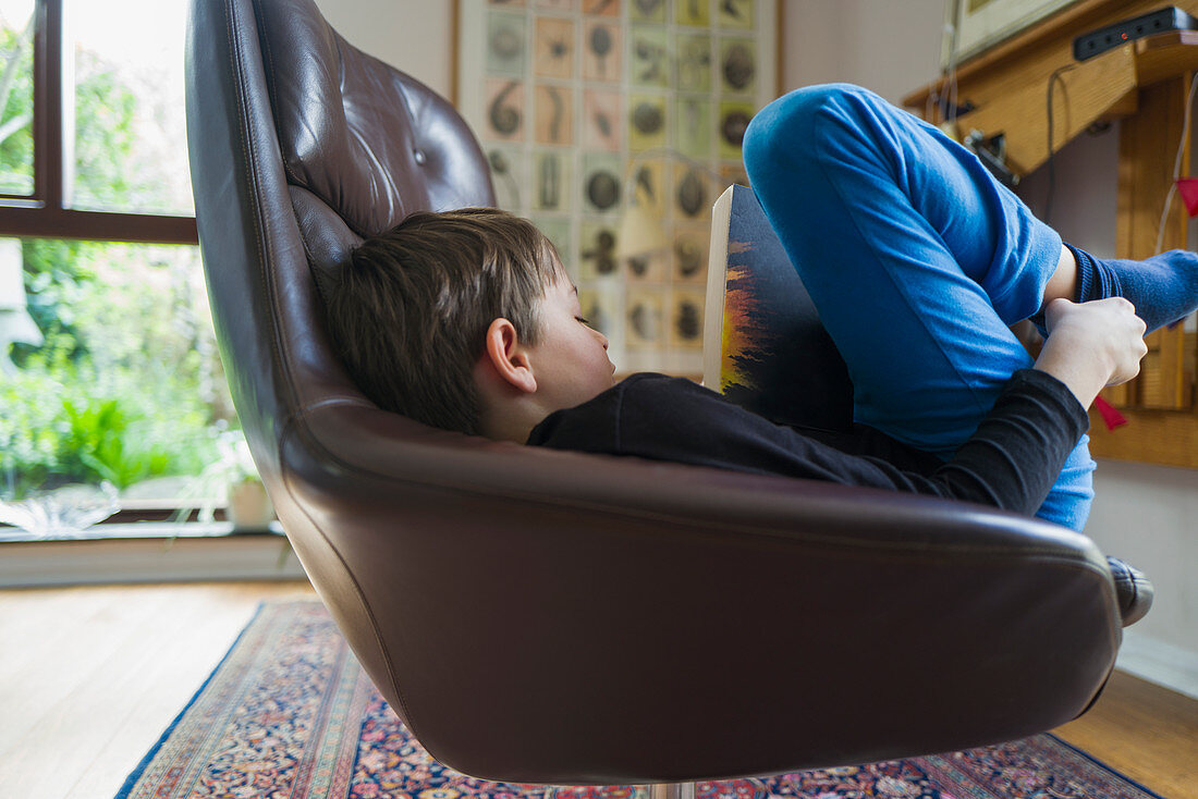 Boy reading book in leather armchair