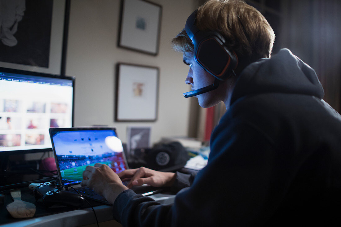 Boy playing videogame at laptop in dark room