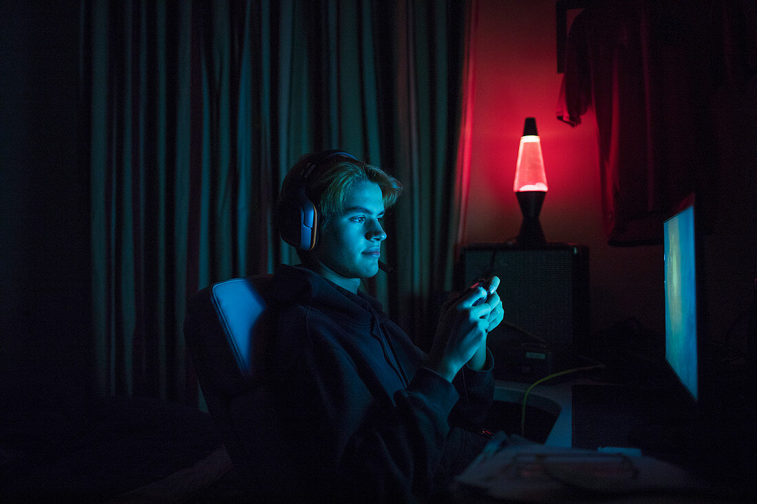 Boy in headset playing videogame in dark bedroom