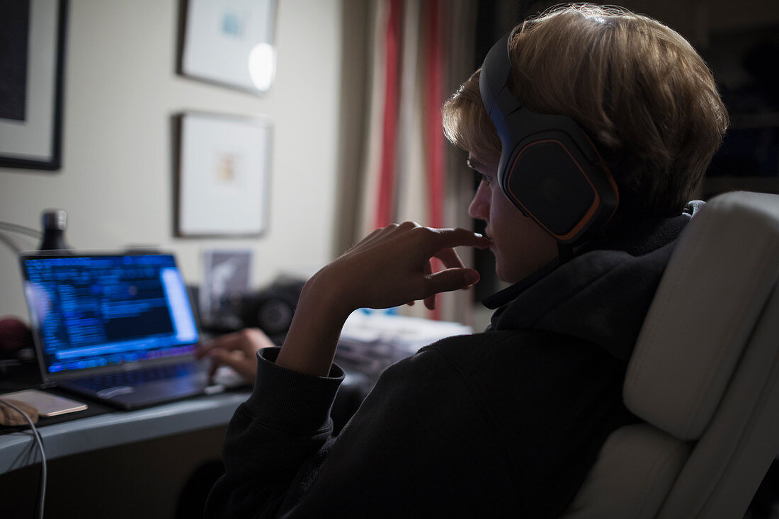 Teenage boy using computer in dark bedroom