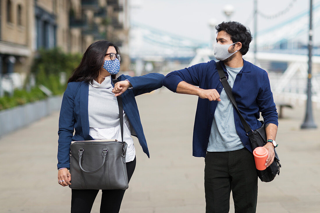 Business people in face masks touching elbows
