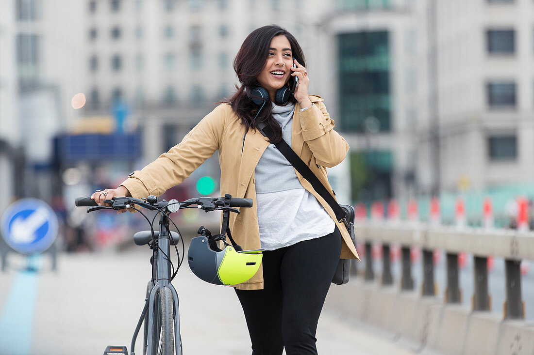 Woman with bicycle talking on smart phone in city