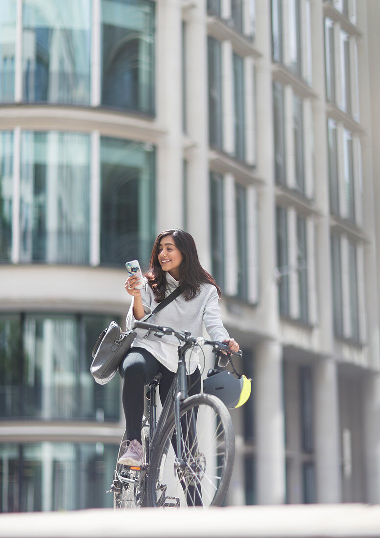 Woman using smart phone on bicycle in city