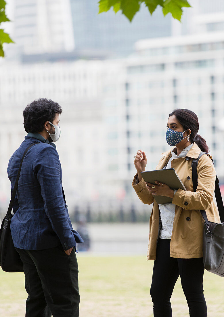 Business people in face masks talking in city park