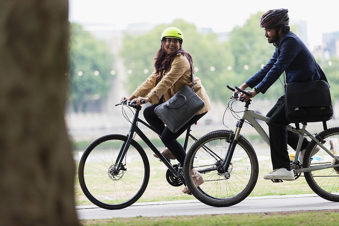 Happy couple in helmets riding bicycles in park