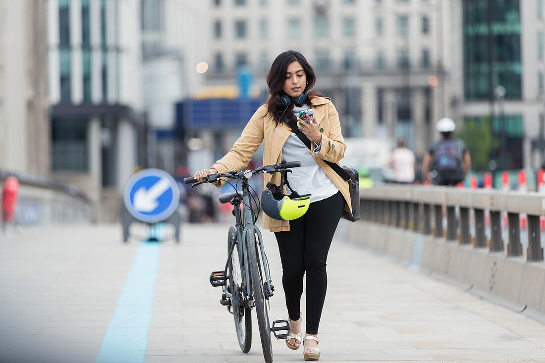 Businesswoman with smart phone walking bicycle