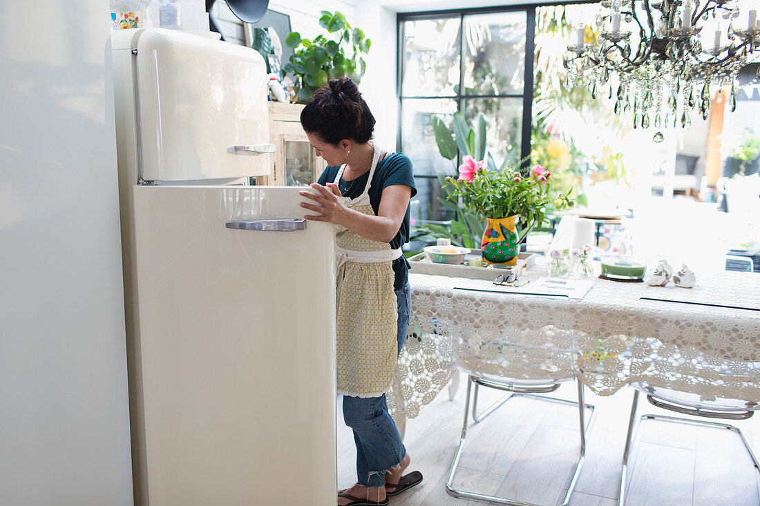 Woman in apron standing at open refrigerator