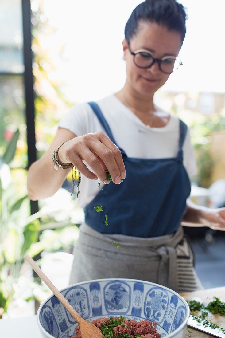 Woman sprinkling fresh herbs over bowl