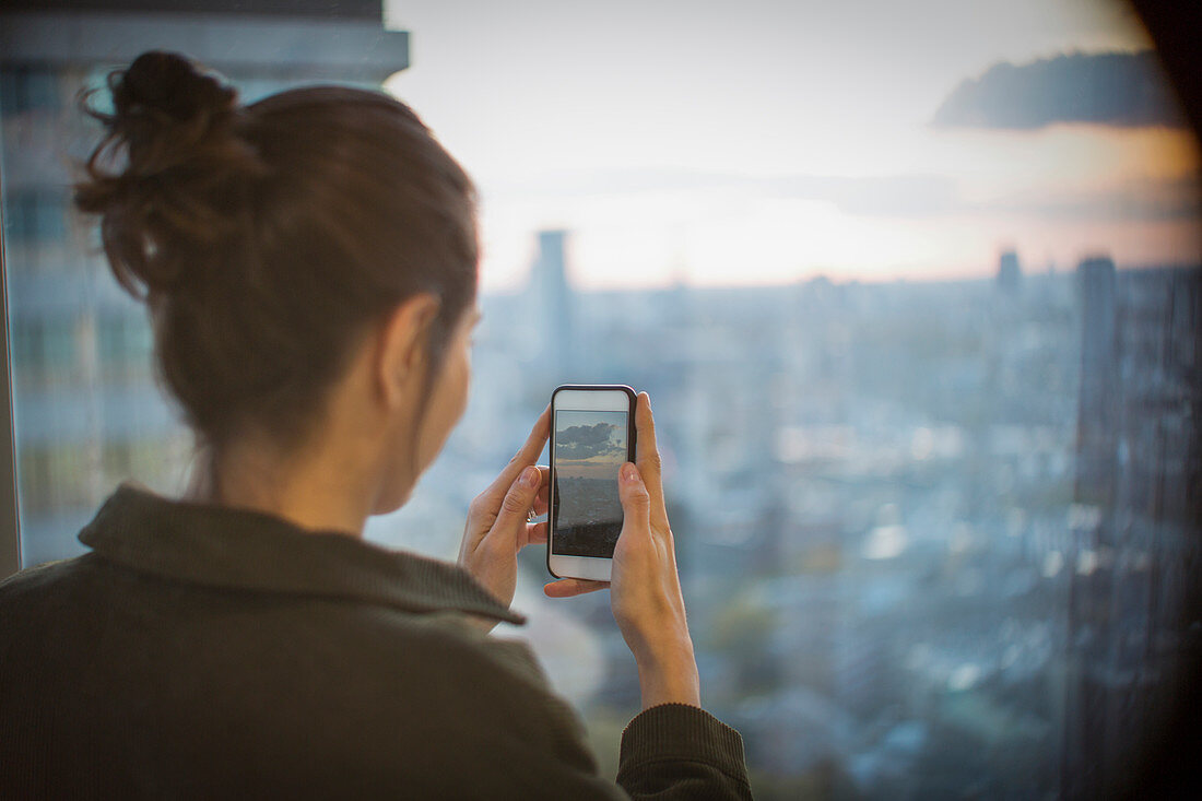 Businesswoman photographing sunset over city