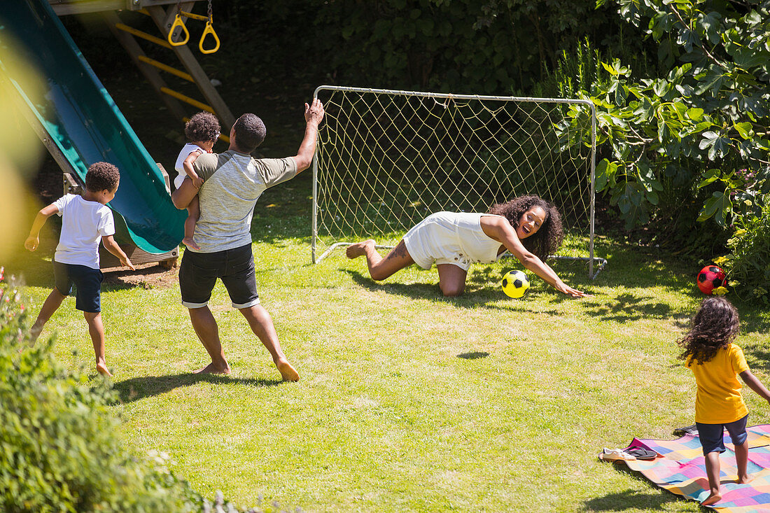 Happy family playing soccer in summer backyard