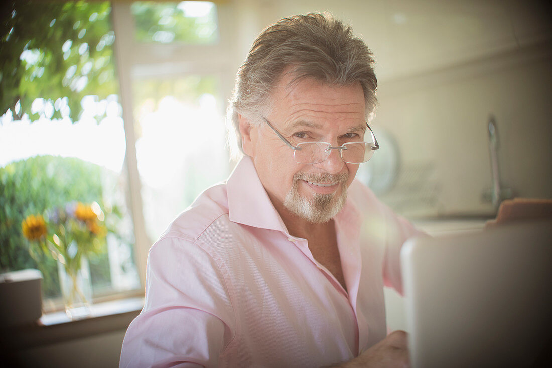 Smiling senior man working at laptop in kitchen