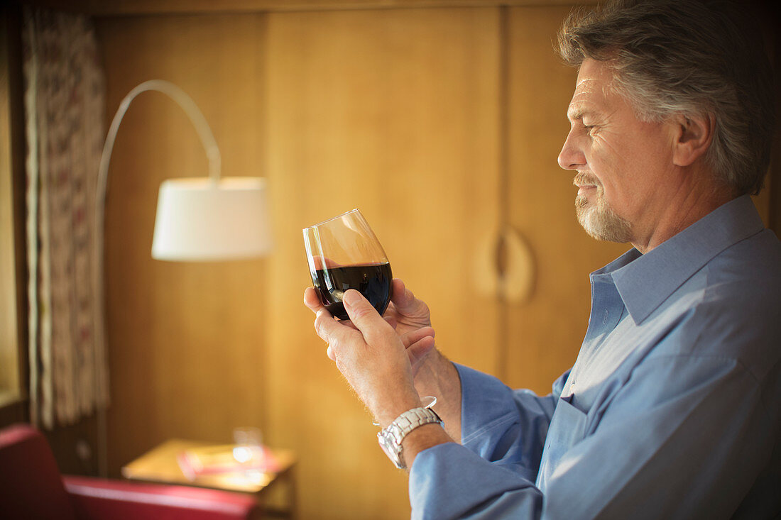 Senior man tasting red wine in living room