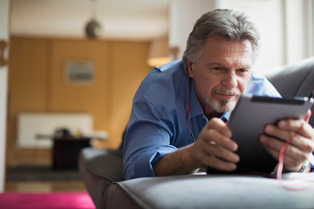 Senior man using headphones and tablet on sofa