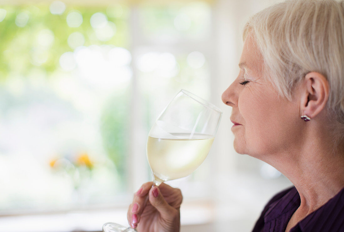 Senior woman smelling and tasting white wine