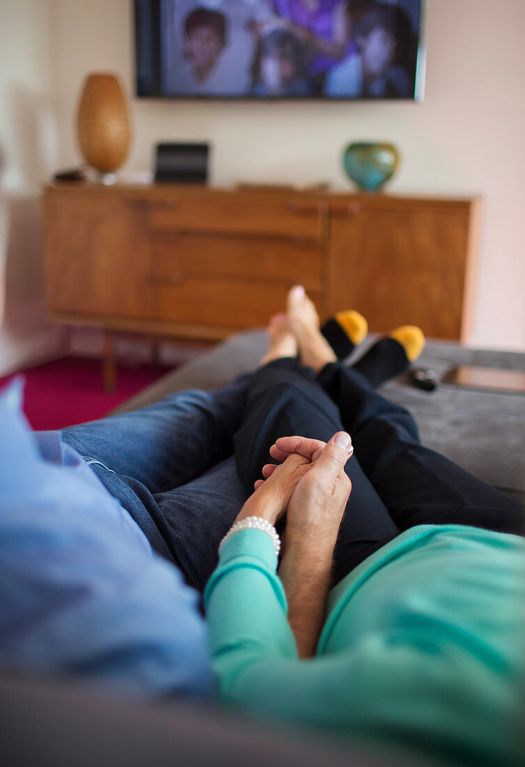 Couple holding hands and watching TV on sofa