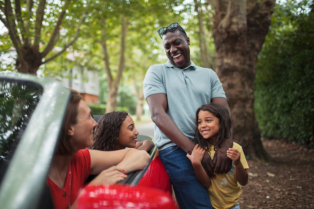 Happy family laughing at convertible in driveway