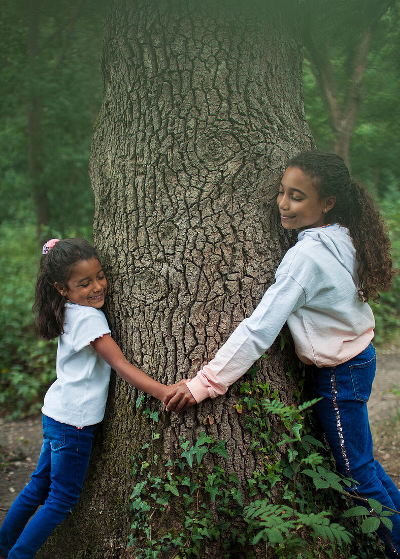 Sisters holding hands and hugging tree trunk