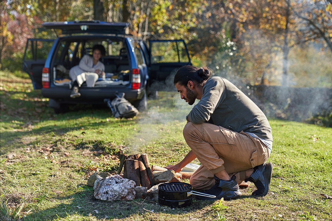 Man preparing campfire outside car in autumn field