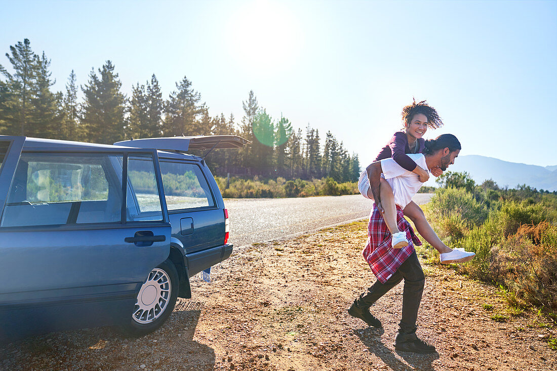 Couple piggybacking outside car at roadside