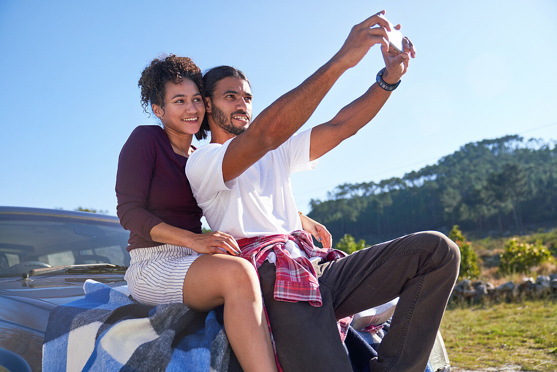 Couple taking selfie on hood of car at roadside