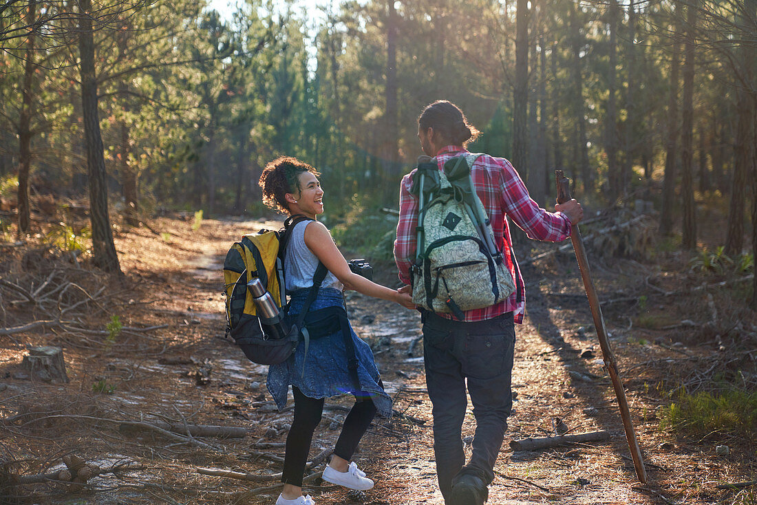 Happy couple with backpacks hiking in sunny woods