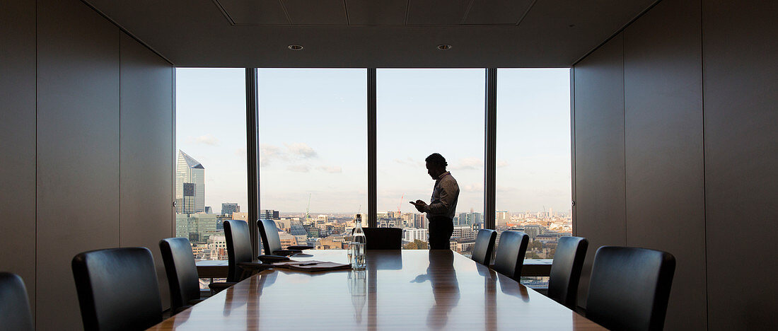 Businessman using smart phone at highrise window