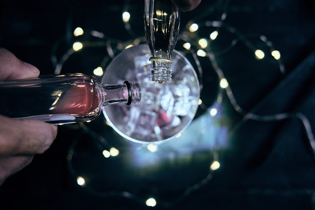 Bartender pouring various drinks from bottles into shaker with ice cubes