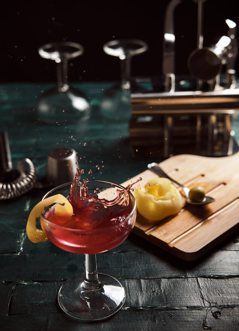 Roter Cocktail mit Zitronenschale auf Bartheke