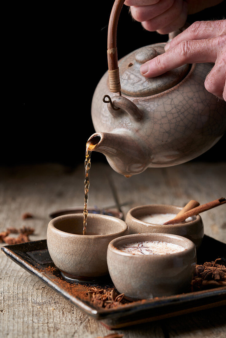 Masala Chai aus Teekanne in Keramikschalen giessen