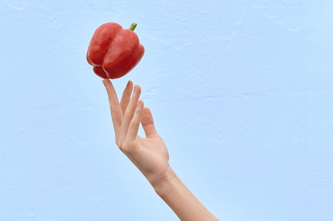 Crop woman tossing fresh red pepper in air showing concept of healthy diet on blue background