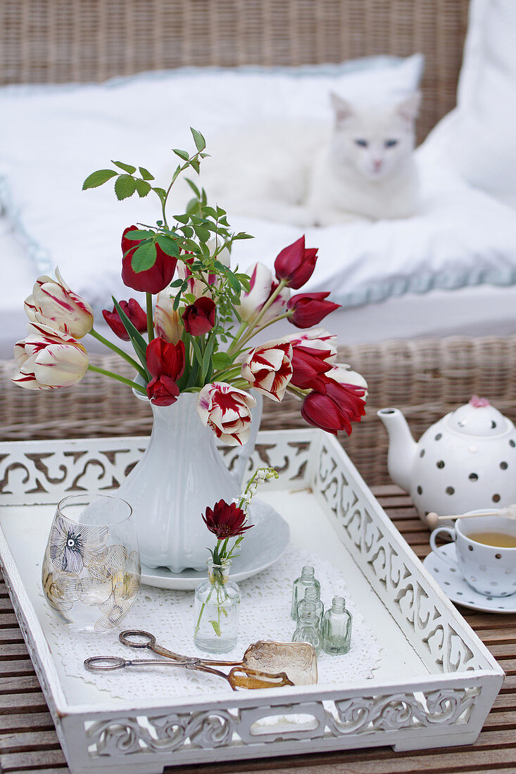 Bouquet of tulips with a wild rose branch on a white wooden tray