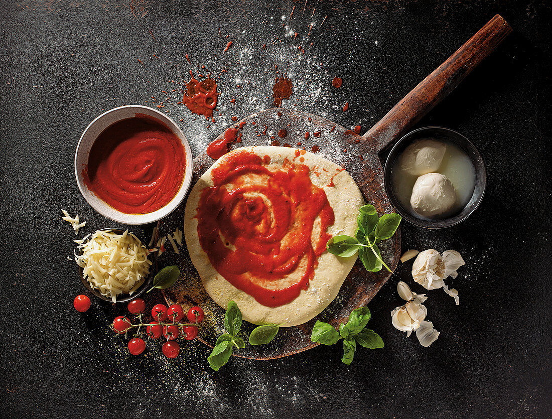 Pizza base with tomato sauce next to mozzarella, garlic and basil
