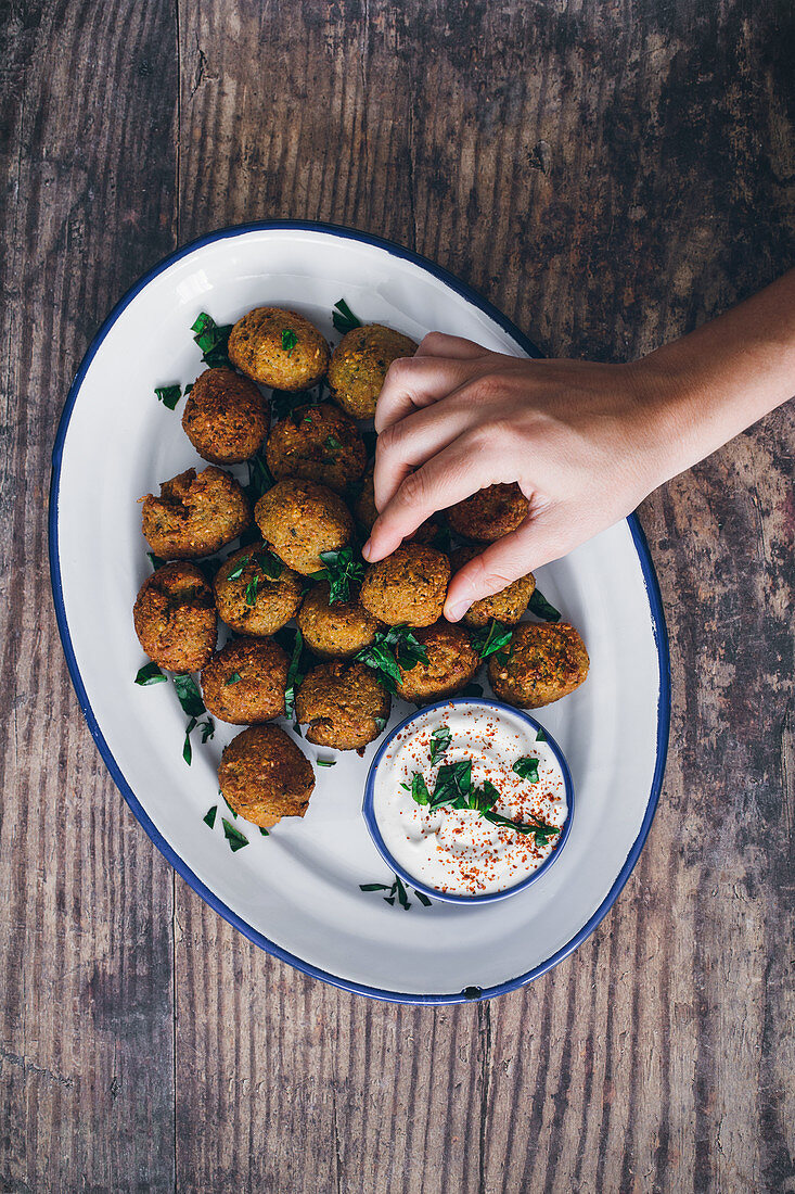 Hand treating with golden fried legume falafel with sauce on wooden table