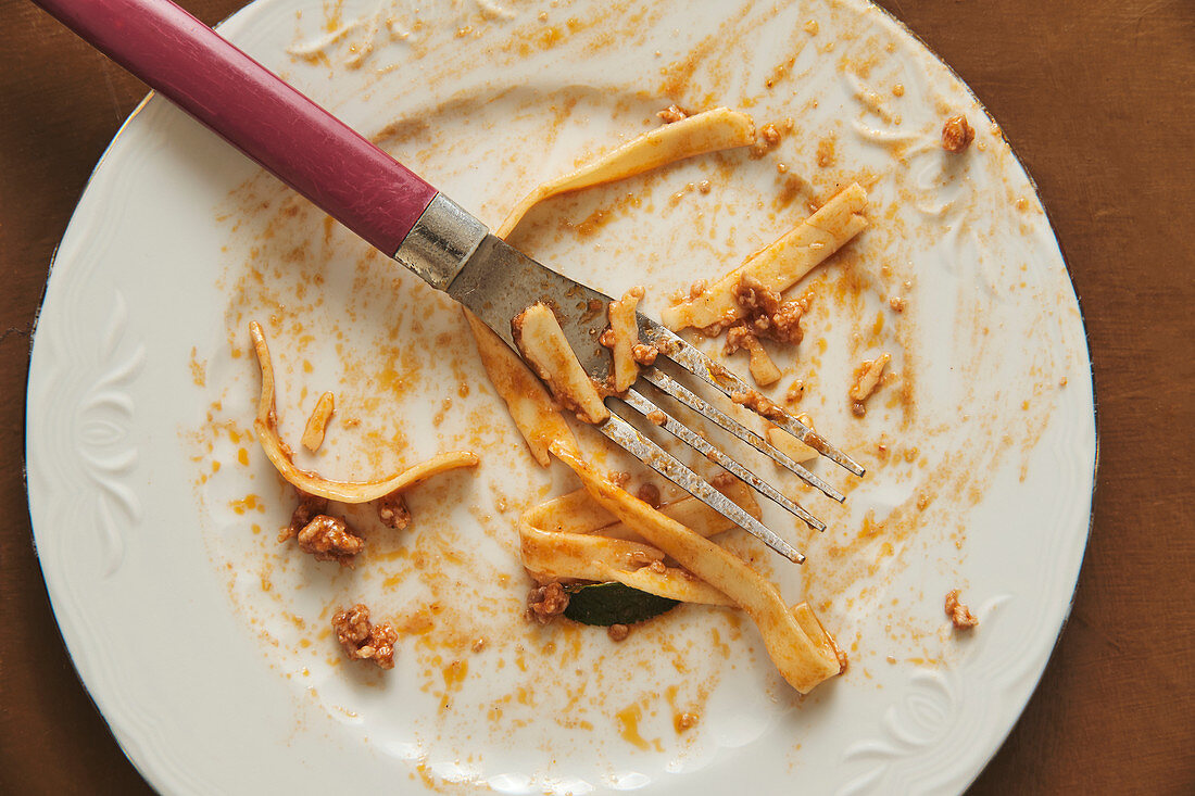 Empty white plate and fork smeared with food after eating delicious Bolognese pasta