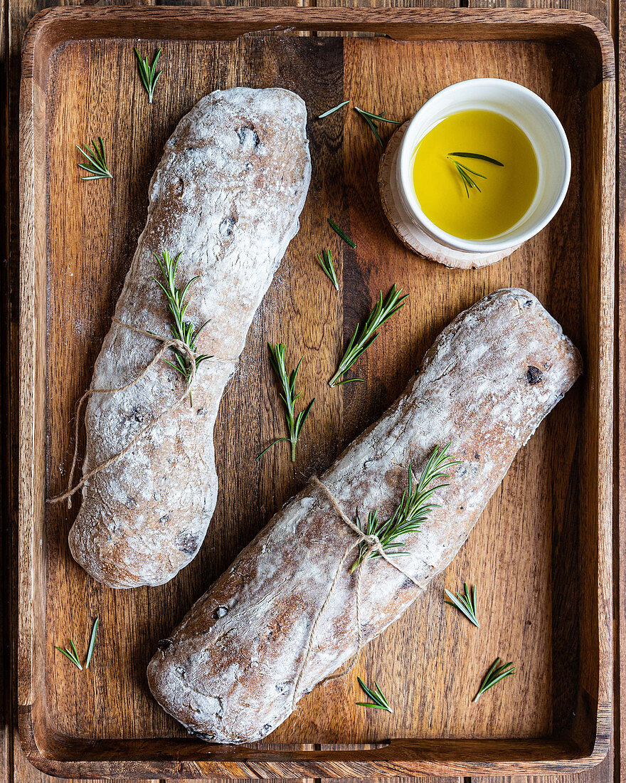 Italian ciabatta bread served on wooden tray with pot of olive oil and fresh rosemary