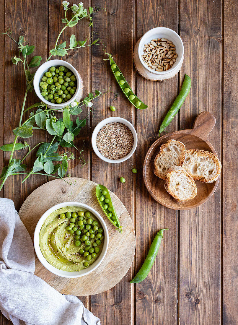 Hummus made with green pea on wooden table with ingredients and bread slices