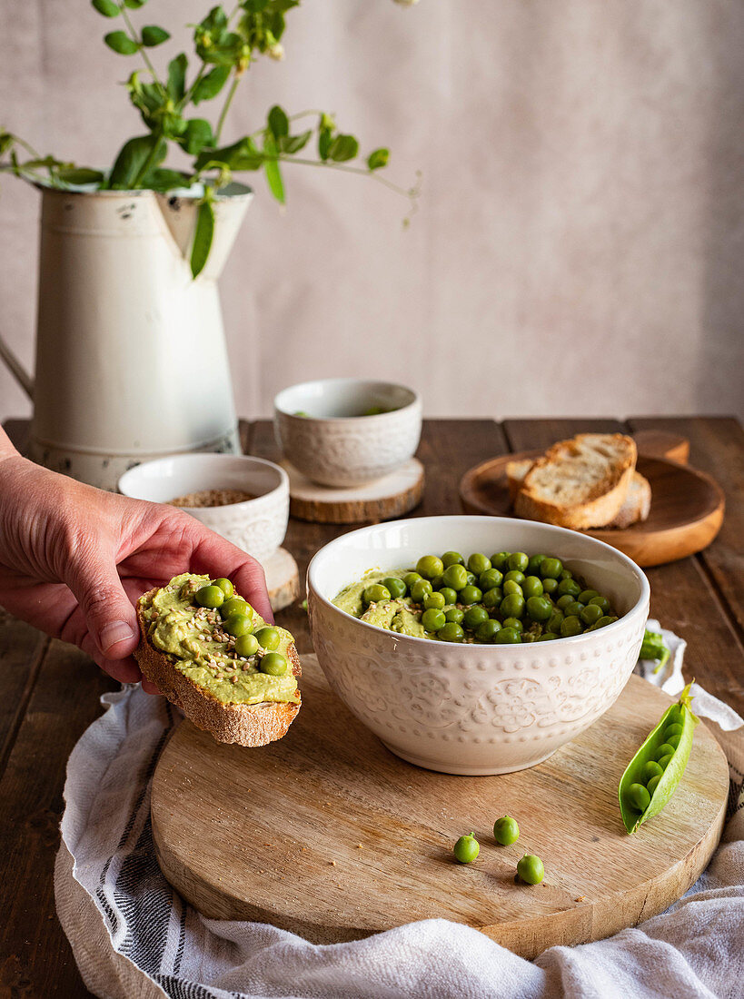 Hand holding tasty healthy toast with homemade green pea hummus