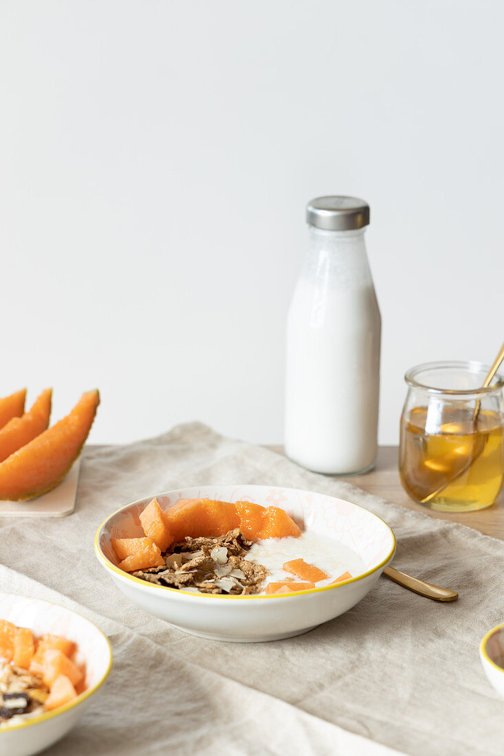 Bowls with delicious healthy breakfast prepared with yogurt and granola with fresh cantaloupe melon served on table with ingredients