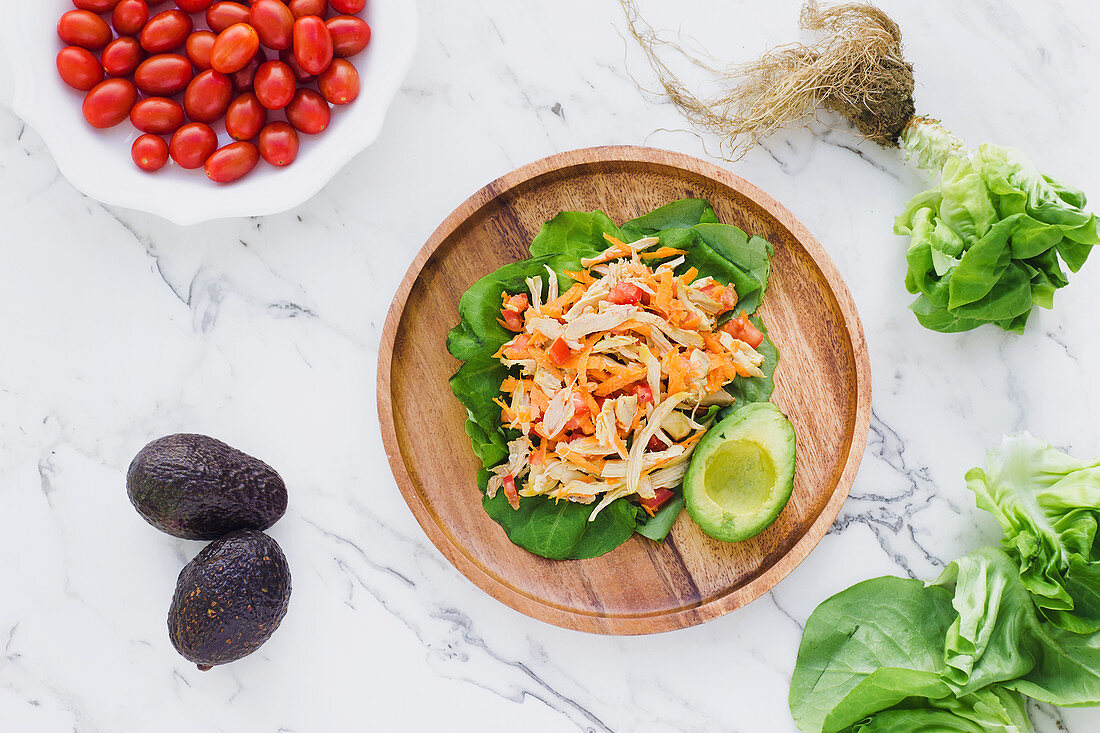 Chopped chicken mixed with cut cherry tomatoes on fresh lettuce leaves near half of avocado